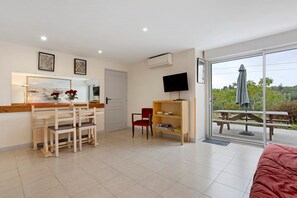 Une pièce comprenant une table à manger, des chaises, un téléviseur et une porte-fenêtre coulissante donnant sur un espace extérieur.