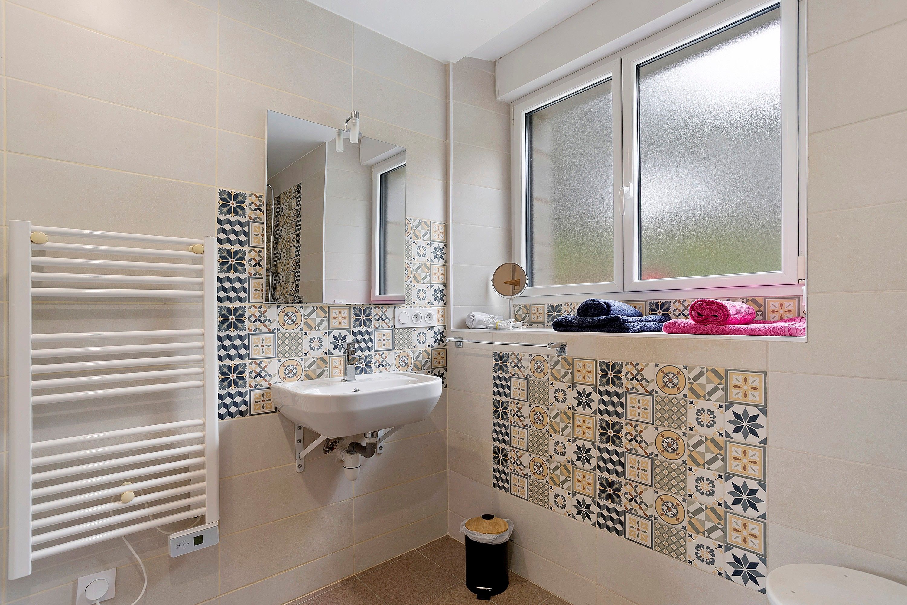 Een badkamer met een wit wastafelmeubel, een spiegel, een handdoekrek en een raam.