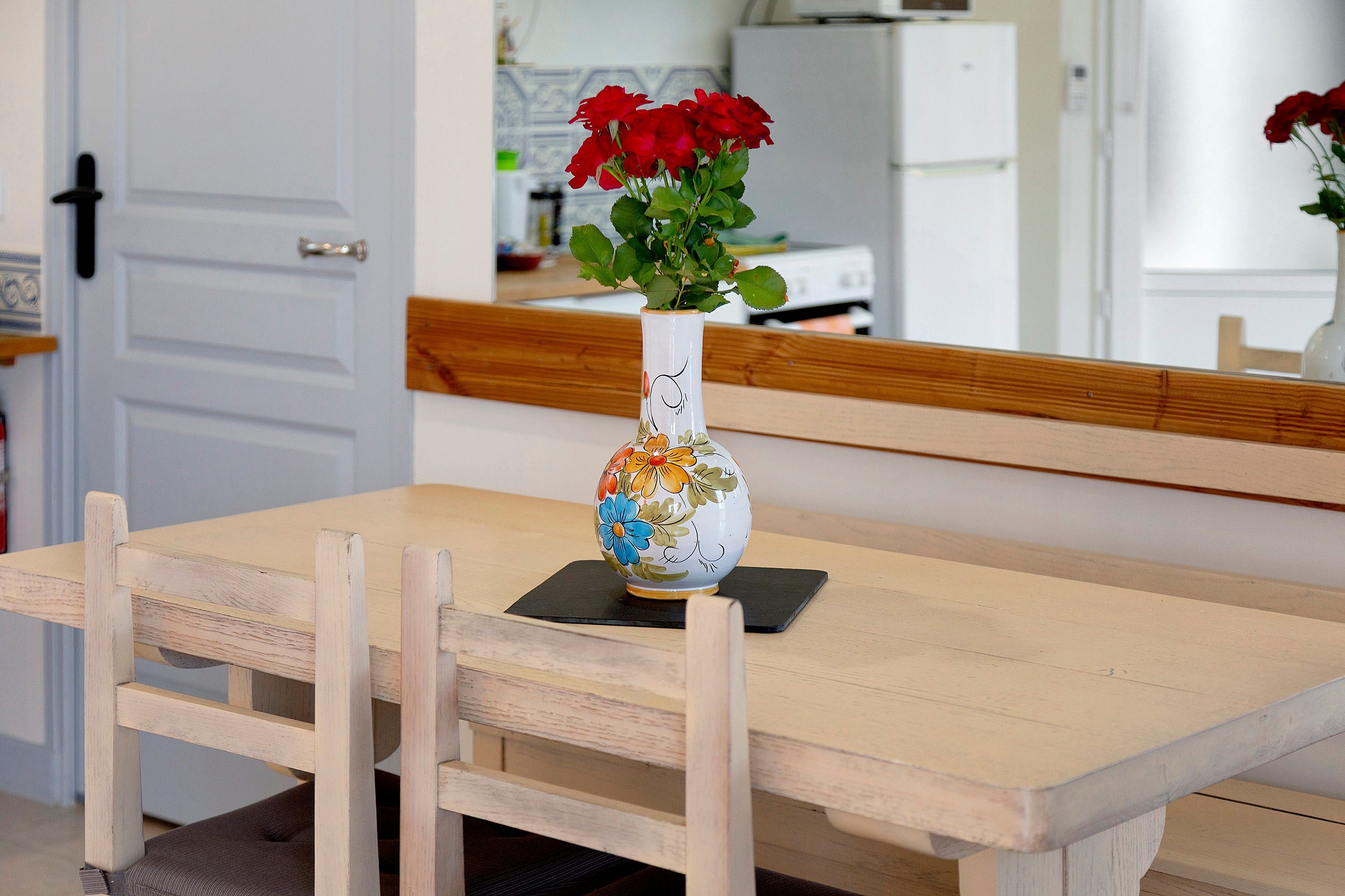 A dining table with a vase of red flowers and a decorative bowl with floral patterns.