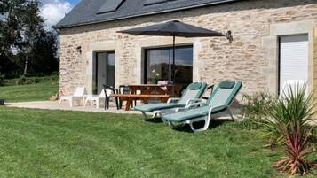 A stone building with a patio, a table, chairs, and two lounge chairs.