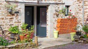 A stone building with a dark door, potted plants, and a brick wall.