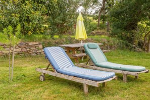 Two lounge chairs with striped cushions on a wooden table, a yellow umbrella, and a stone wall in a garden setting. - Apartment 'Ty Sterenn' with private garden, Wi-Fi and air conditioning (Bannalec)
