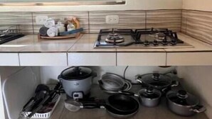 Une cuisine équipée d’une cuisinière à gaz, d’un four encastré et de divers ustensiles de cuisine et casseroles rangés dans les placards sous le plan de travail.