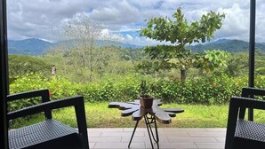 Une terrasse avec deux chaises et une table, offrant une vue sur un paysage luxuriant, avec des arbres et des montagnes à l’horizon.
