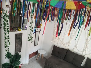 A room with a sofa, a small table, and a mirror. There are plants and colorful ribbons hanging from the ceiling.