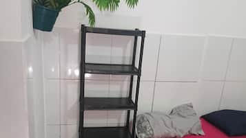 Una habitación con cama, una estantería metálica negra, un tapete estampado, una planta en maceta y una pared con cuadros.