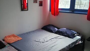 Un dormitorio con cama, una mesita y una ventana con cortinas.