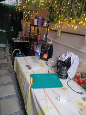 A table with a teal cutting board, a kettle, a water bottle, and a coffee maker.