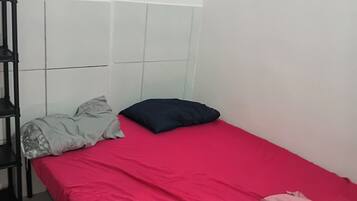 Una habitación pequeña con cama individual, colcha roja, estante negro y piso estampado.