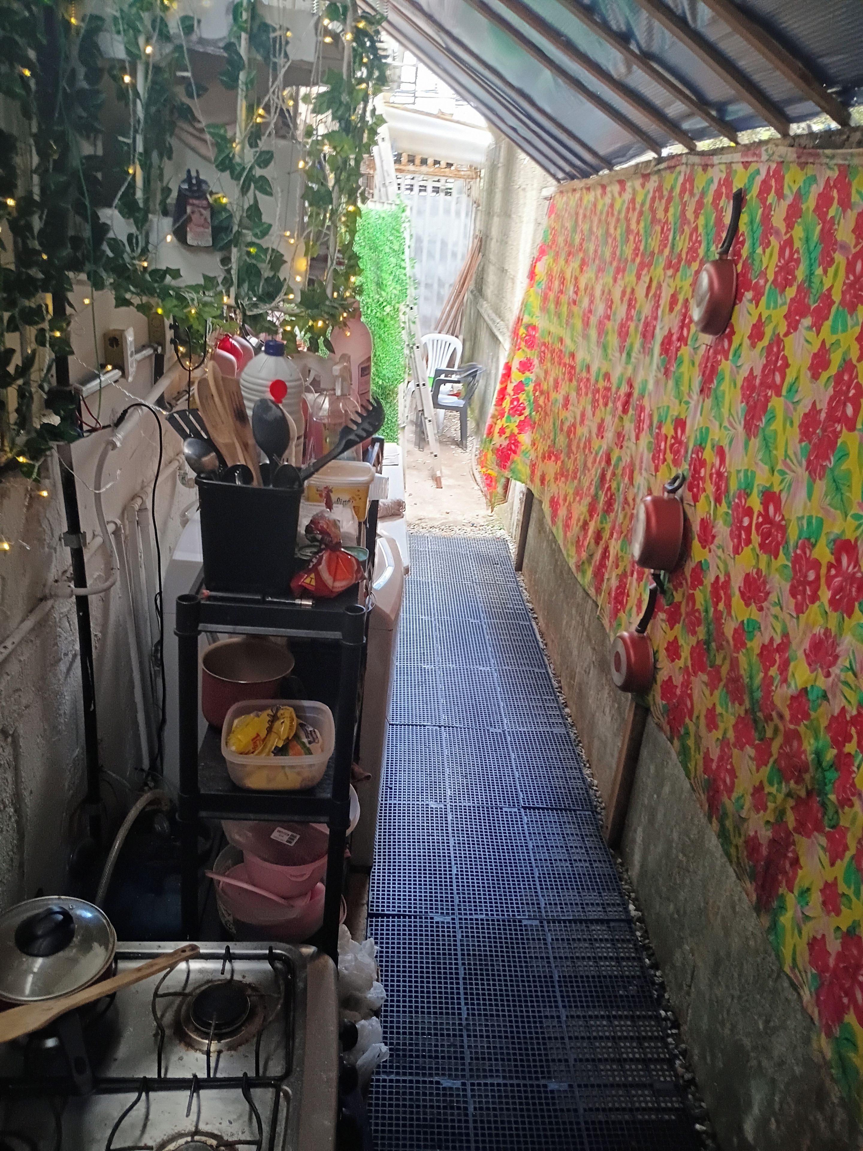 Un pasillo estrecho con piso de rejilla metálica, un estante con utensilios de cocina y una pared con estampado floral.