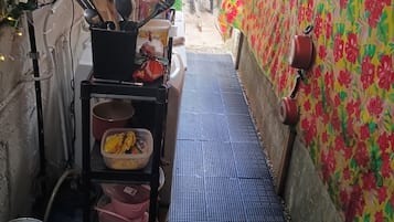 Un pasillo estrecho con piso de rejilla metálica, un estante con utensilios de cocina y una pared con estampado floral.