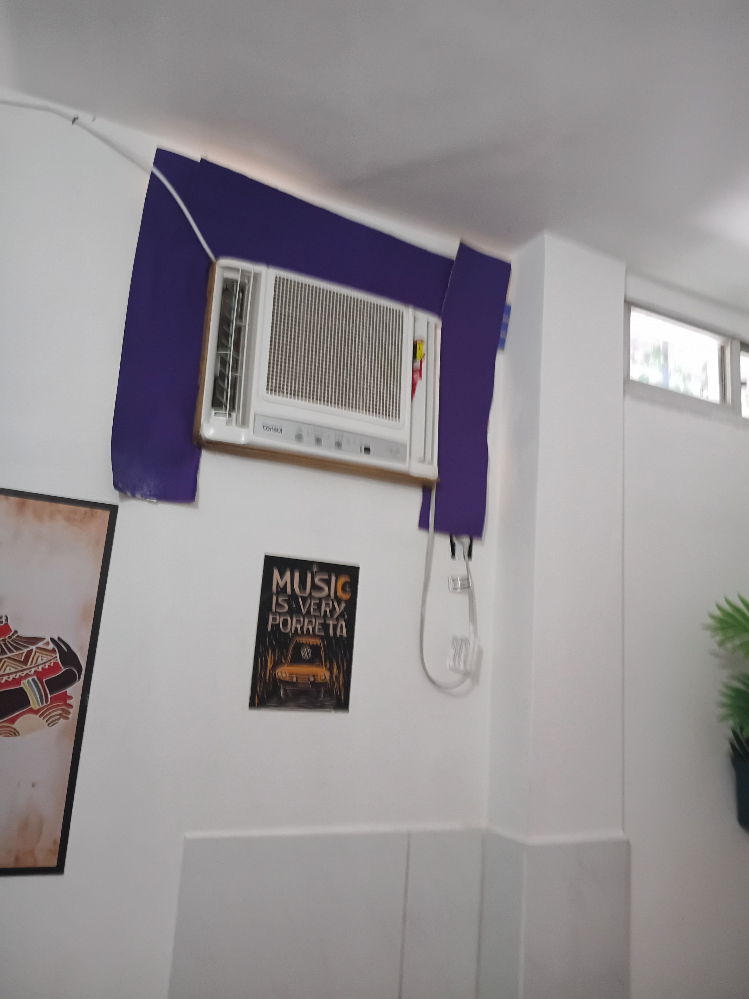 A room with a white wall, a mounted air conditioner, a wall-mounted phone, and a poster.