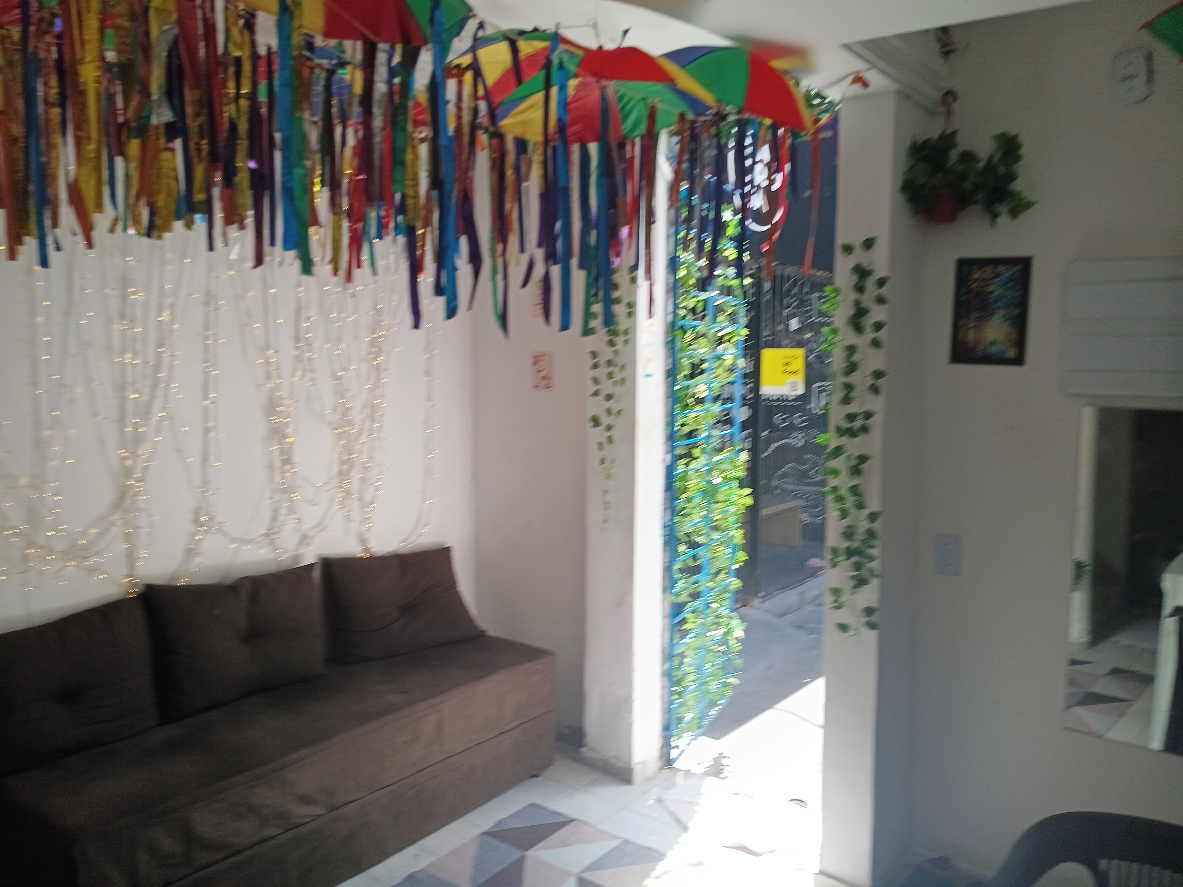 Quarto com sofá marrom, parede branca e porta com planta verde.