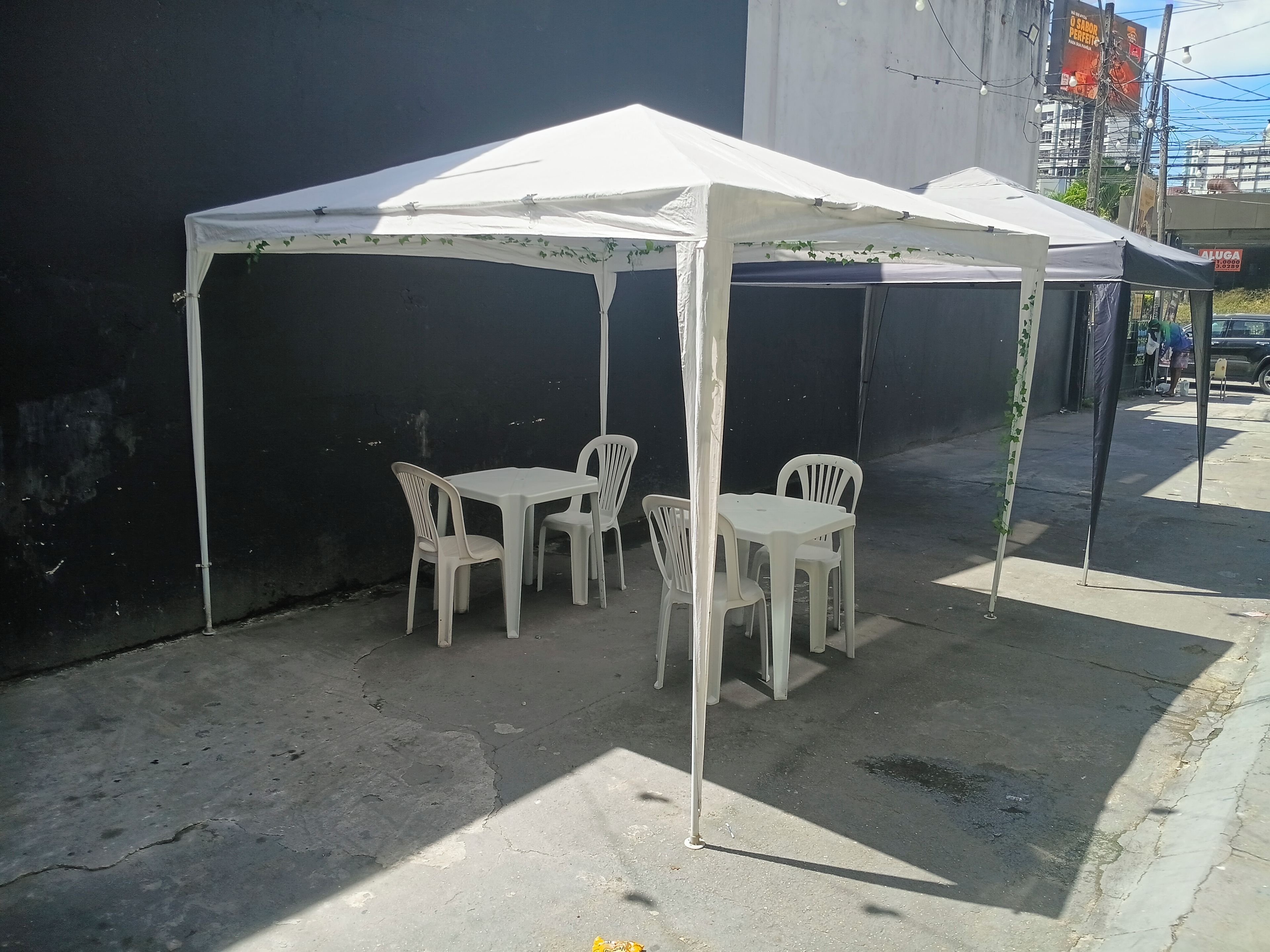 A white outdoor tent with a table and chairs, set against a dark wall.