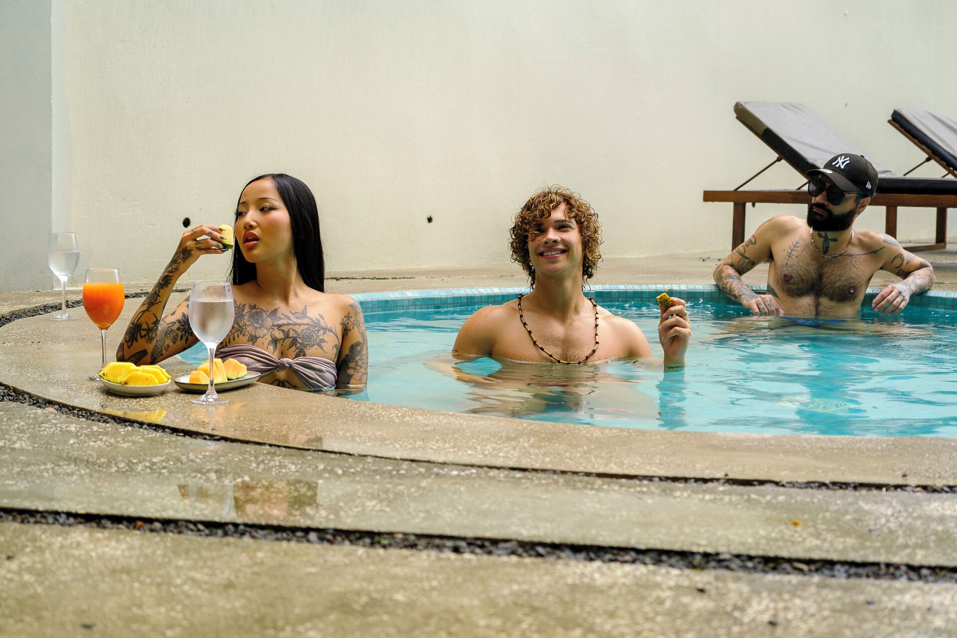 A pool area with lounge chairs and a table with drinks and fruit.