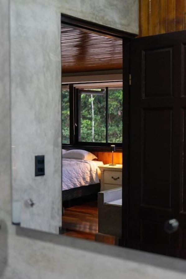 Un dormitorio con cama, mesita de noche y ventana con vistas a la vegetación.