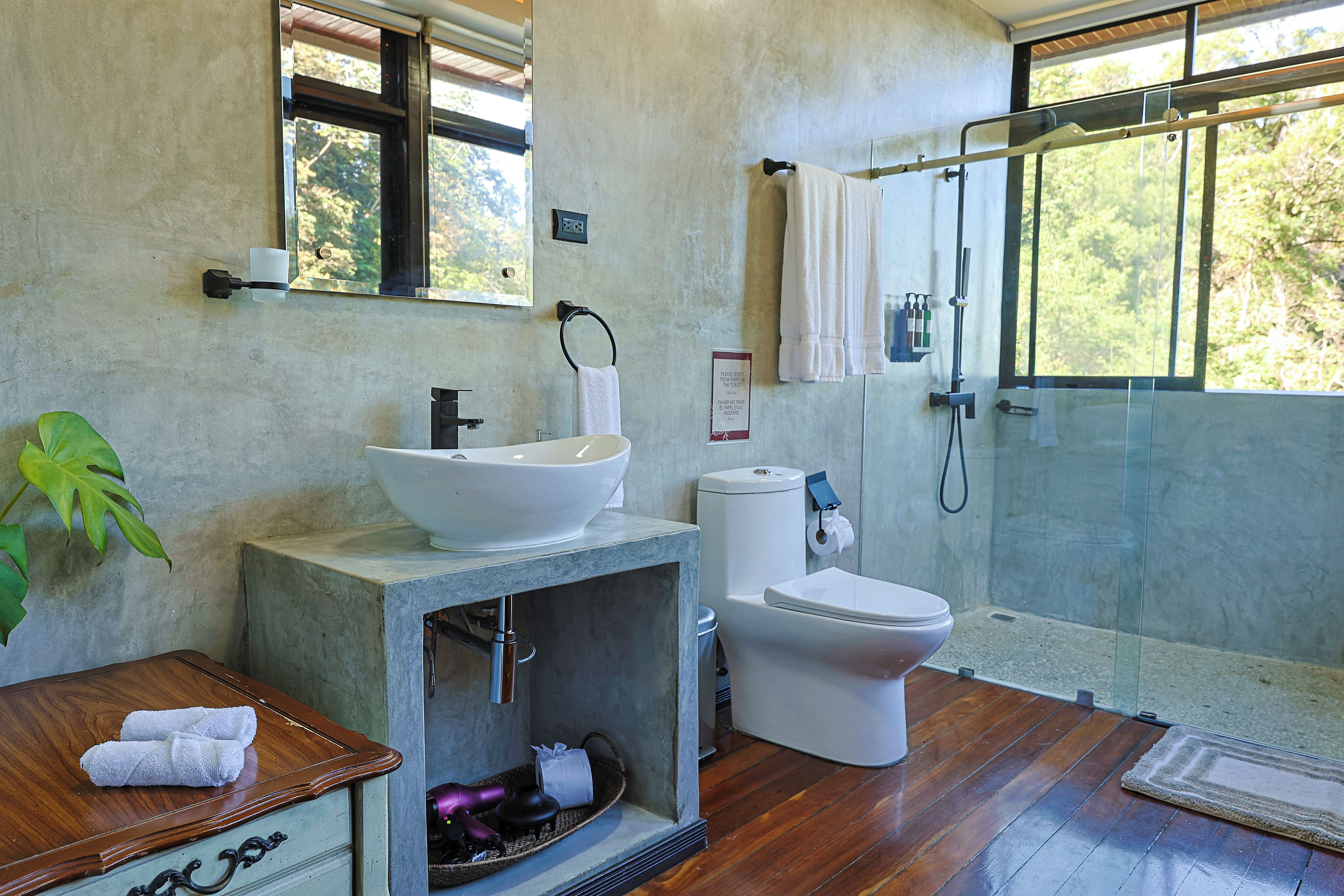 A bathroom with a large window, a sink, a toilet, and a shower area.