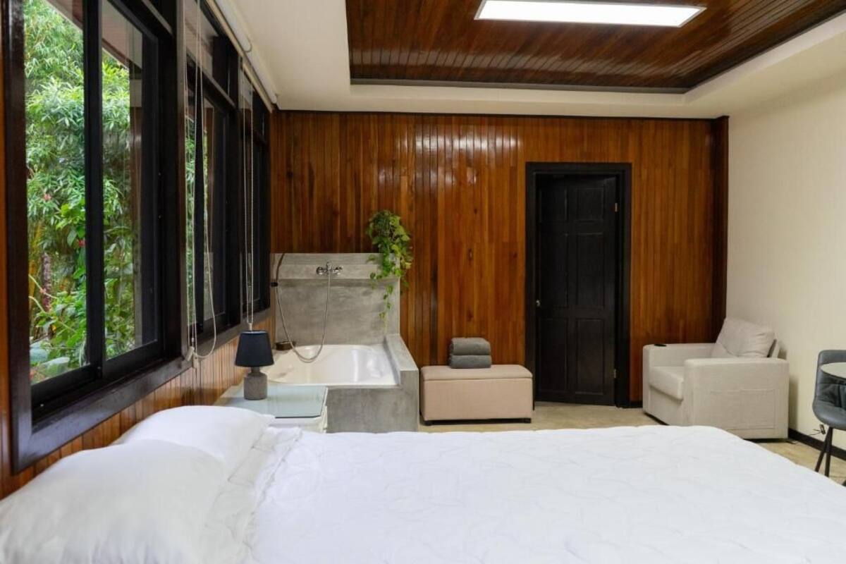 A bedroom with a large bed, a bathtub, and a seating area.