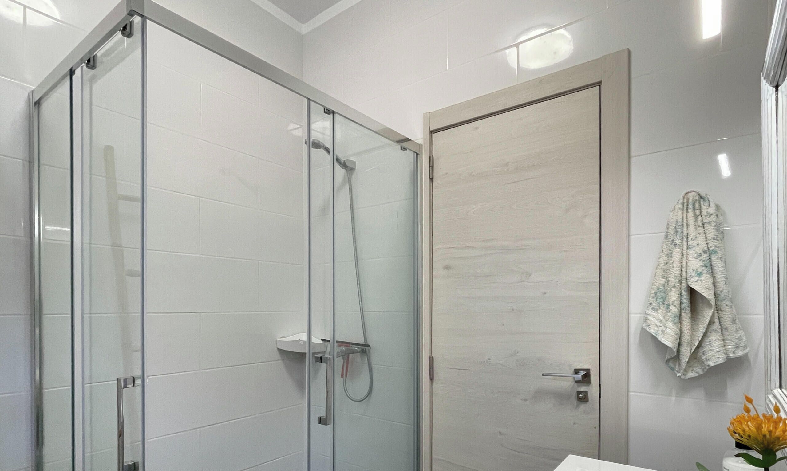 A modern bathroom with a glass-enclosed shower, a wooden door, and a towel hanging on the wall.