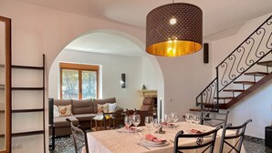 Un comedor con una mesa preparada para cuatro, una escalera y una sala de estar al fondo.