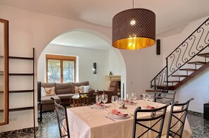 Ein Essbereich mit einem Tisch für vier Personen, eine Treppe und ein Wohnzimmer im Hintergrund.