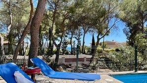 Un área de piscina con sillas de descanso, una valla y árboles.