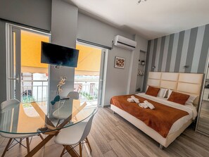 A modern hotel room with a glass dining table, a bed with a striped headboard, and an air conditioning unit. - Stylish Studio Steps from the Acropolis- Cielo Homes (Athina)