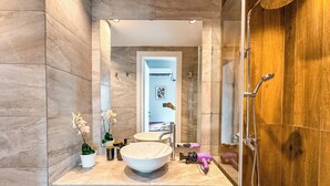 Een moderne badkamer met een marmeren wastafel, een ruime wastafel, een spiegel, een douche en een houten deur.