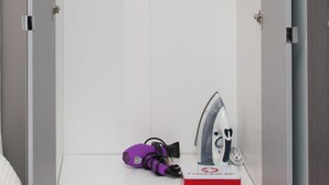 Een witte kast met een kledingroede, een verbanddoos en een paars object op het onderste plankje.