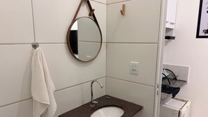 Ett badrum med ett vitt handfat, en spegel, en handdukshängare och ett litet kylskåp.
