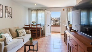 Ett vardagsrum med en soffa, ett matbord, stolar, en tv och en köksdel.