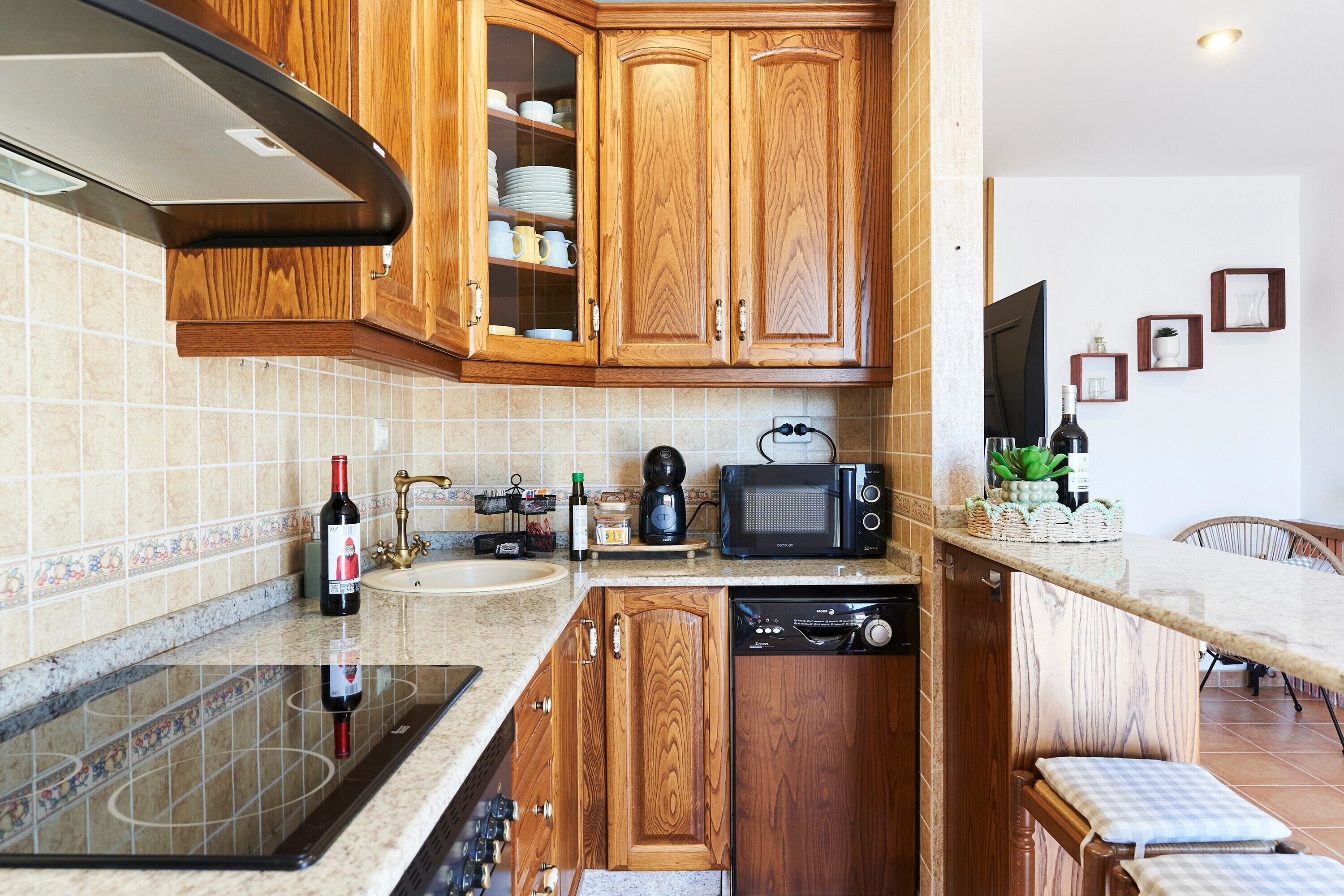 Una cocina con armarios de madera, microondas, cafetera y una botella de vino.