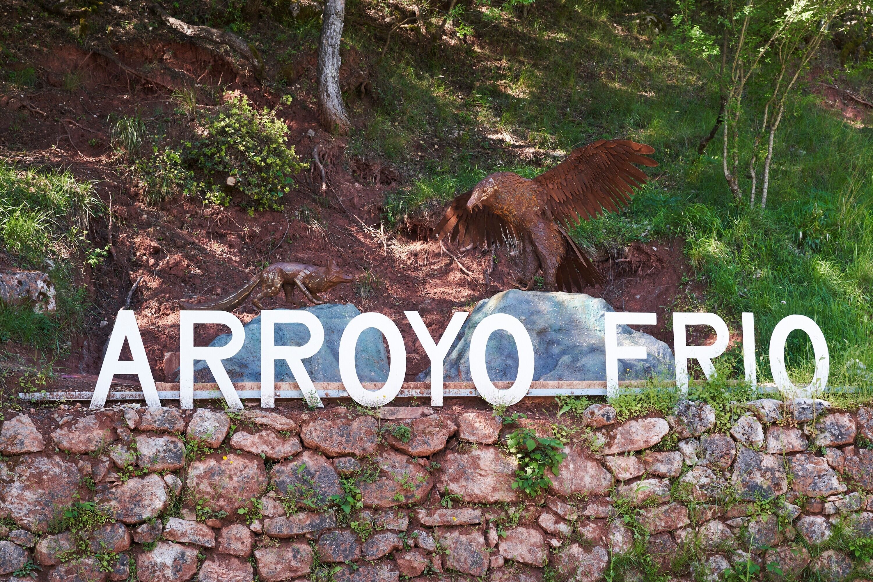 A stone wall with the text 'ARROYO FRIO' and a rocky terrain with sparse vegetation.