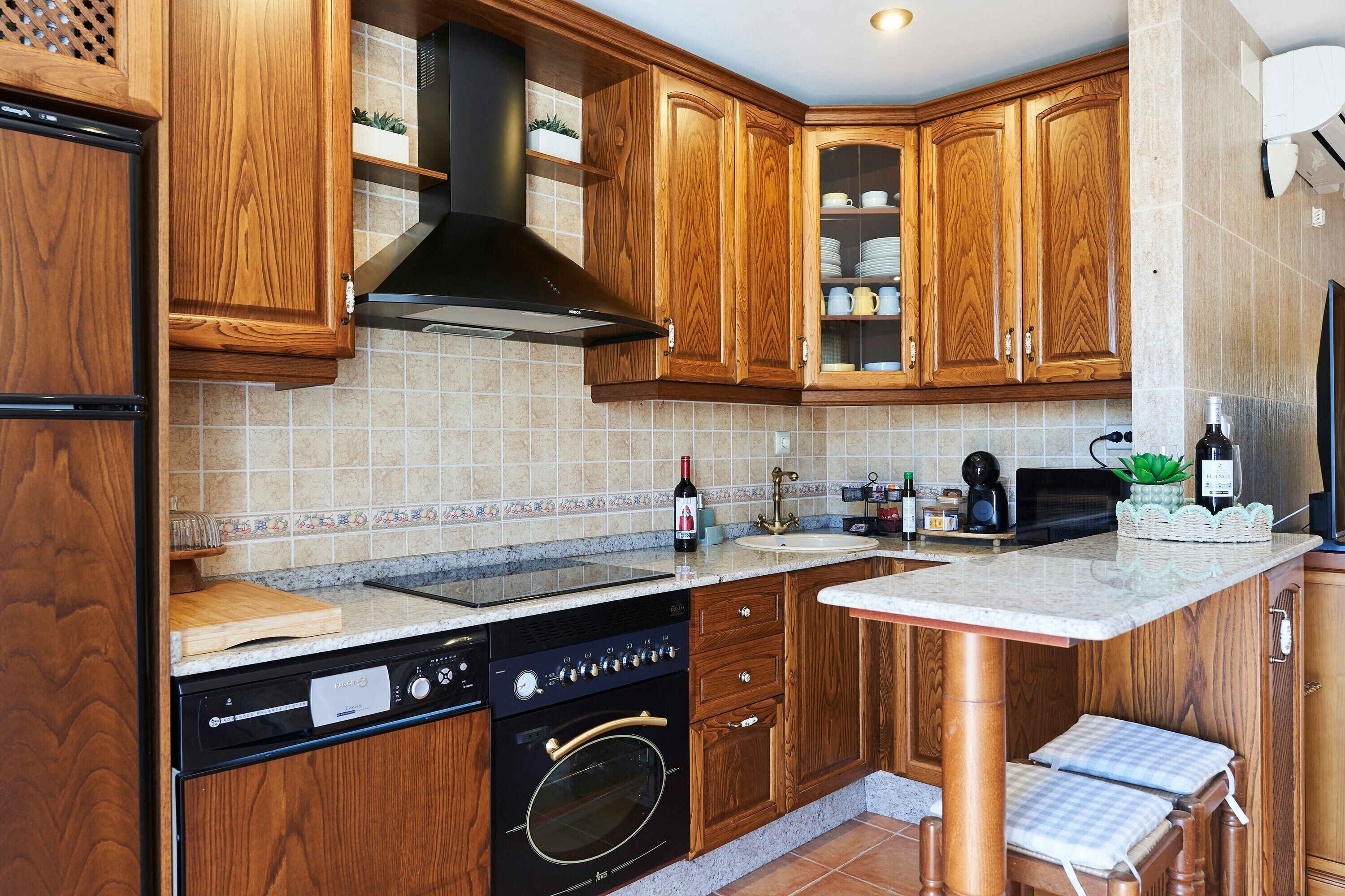 Una cocina con armarios de madera, lavavajillas, horno, lavabo y encimera con una botella de vino.