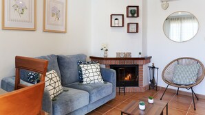 A living room with a sofa, armchair, fireplace, and wall-mounted decor. - Apartment 'Estrella Del Guadalquivir' with Shared Pool, Wi-Fi and Air Conditioning (Arroyo Frio)