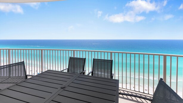 En balkon med et bord og stole, med udsigt over en strand og havet.
