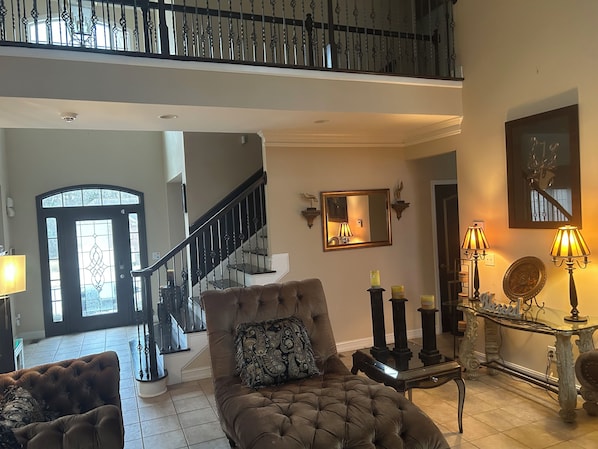 A spacious living area with a grand staircase, a comfortable armchair, and a decorative console table.
