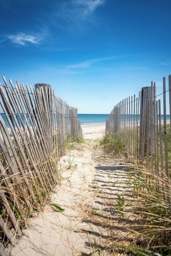 A sandy beach path with wooden fencing, leading to the ocean. - Private Beach Escape - Bay Views & Powder Point Bridge - Duxbury, MA (Duxbury)