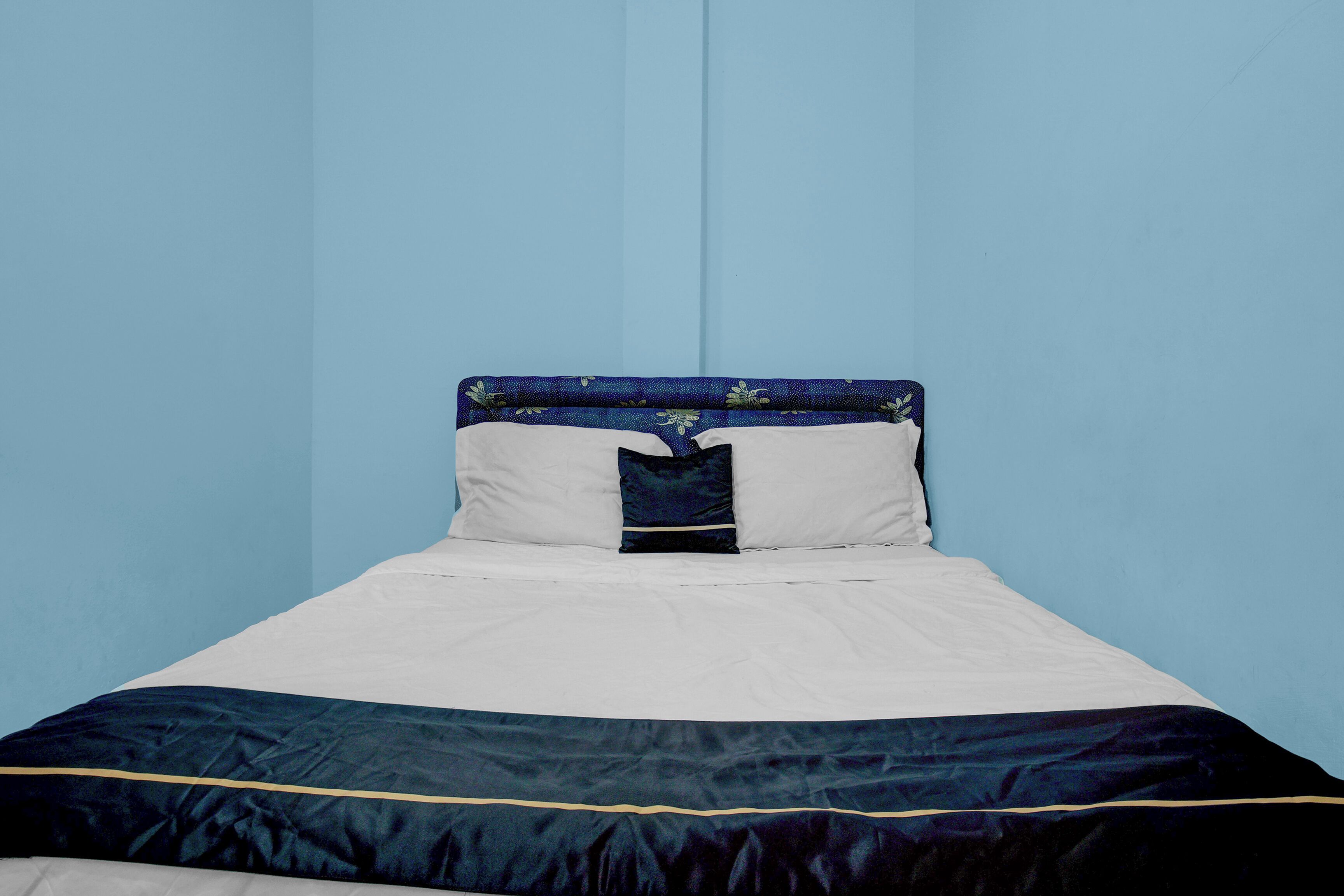 Un lit avec une tête de lit bleue, une literie blanche et une couvre-lit bleu foncé à rayures dorées.