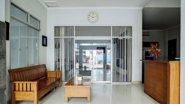 A reception area with a wooden bench, a coffee table, and a clock on the wall. - Hotel O near Palembang Square Mall formerly Wisma Faeyza Syakira (Palembang)