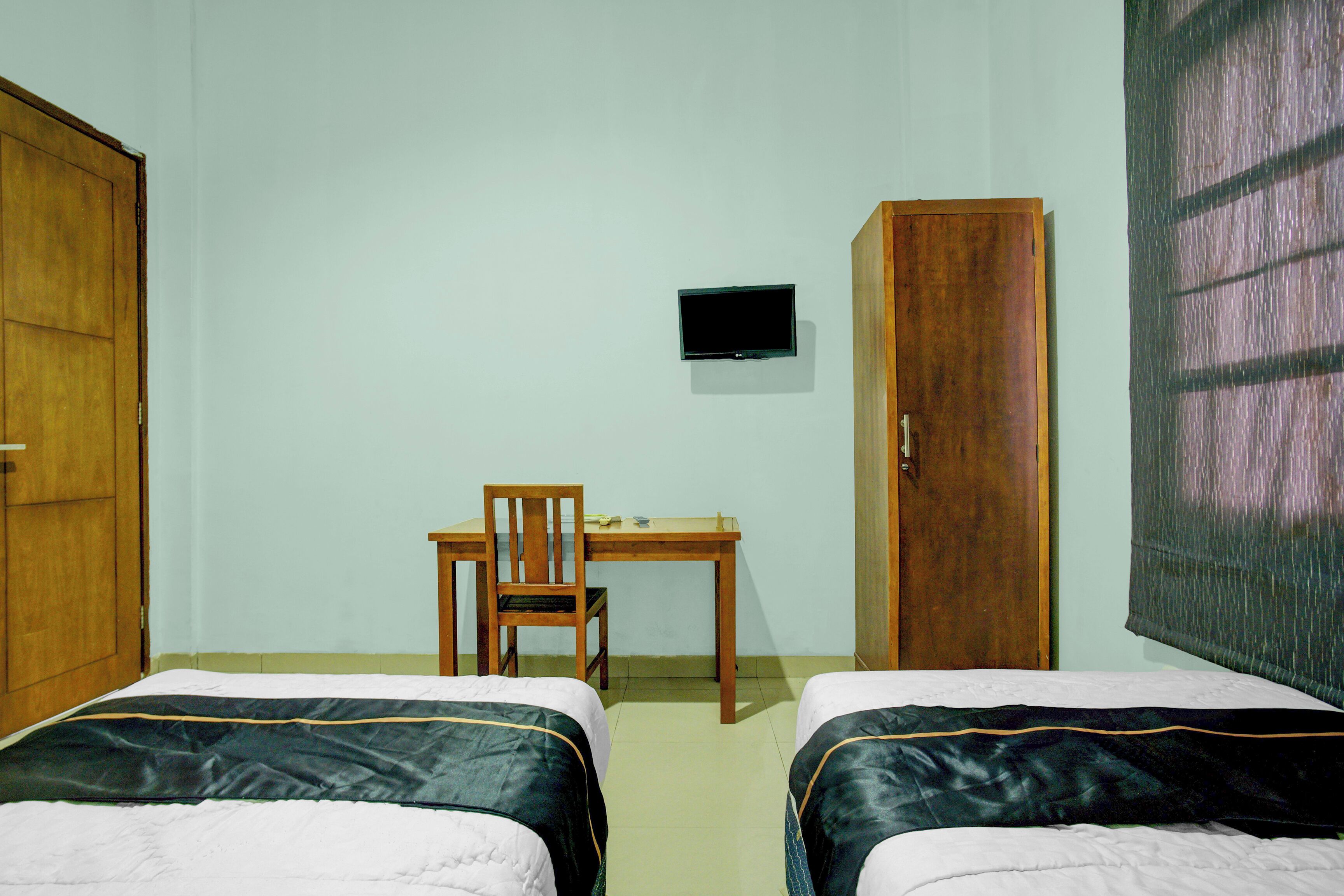 A room with two beds, a desk, a chair, a television, and a wardrobe.