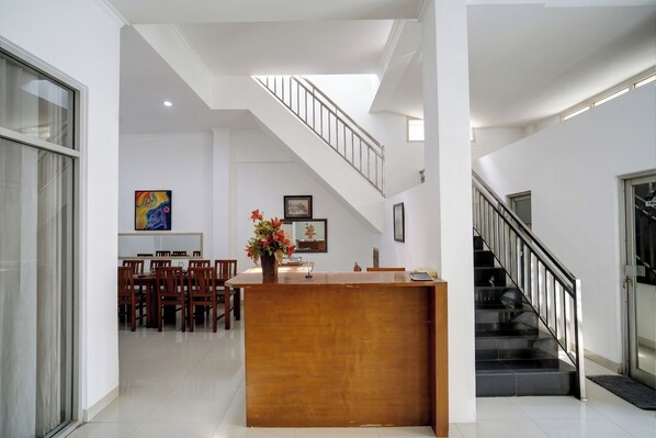 Amplia sala de estar con mostrador de recepción de madera, comedor con sillas, escalera y un gran ventanal.