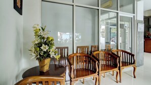A dining area with a round table and wooden chairs, a wicker basket with flowers, and large windows. - Hotel O near Palembang Square Mall formerly Wisma Faeyza Syakira (Palembang)