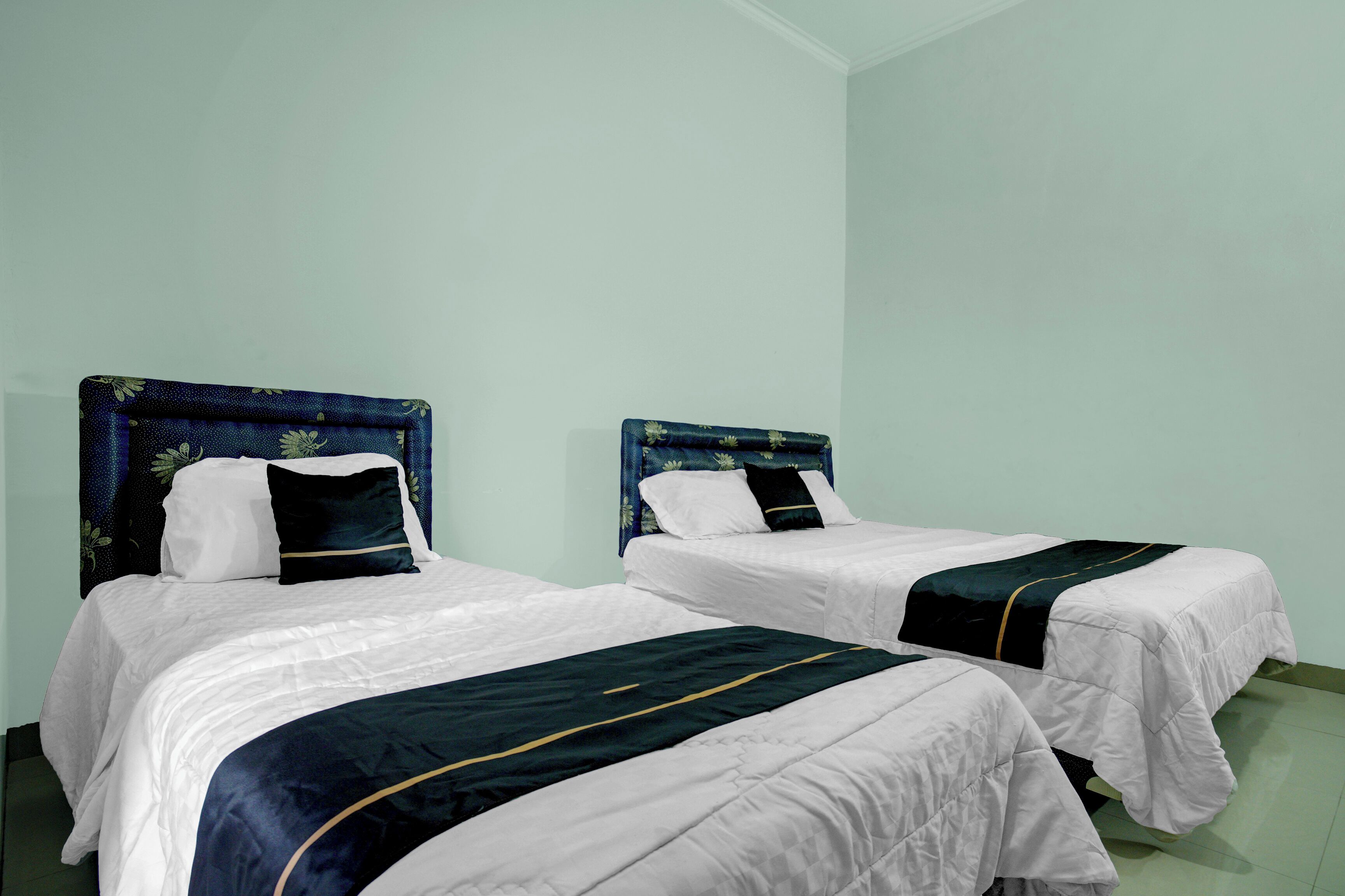 Deux lits simples avec des têtes de lit, du linge de lit blanc et des couvre-lits vert foncé, dans une pièce aux murs vert clair.