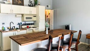 Una cocina moderna con armarios blancos, una isla de madera y un comedor con sillas.