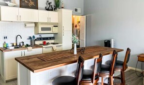 A modern kitchen with white cabinetry, a wooden island, and a dining area with chairs. - Charming 1BR Condo - Top Floor - LAKE VIEW (Village of Four Seasons)