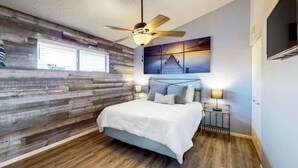 Un dormitorio con cama, ventilador de techo, televisor montado en la pared y un cartel de 'Welcome'.
