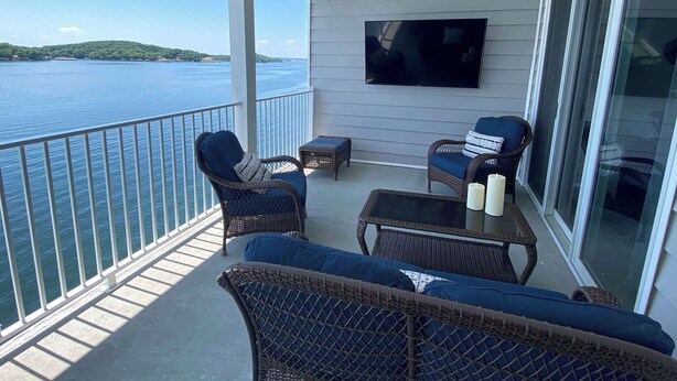 Een balkon met rieten meubilair, een flatscreen televisie en uitzicht op een wateroppervlak.