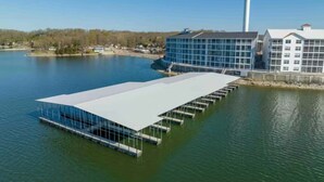 Een groot, rechthoekig gebouw met een plat dak, gelegen op een meer, omgeven door water en een verre oever met bomen en gebouwen.