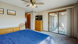 A bedroom with a bed, a wooden dresser, a ceiling fan, a TV, and a sliding glass door to a balcony. - Charming 2BR Condo - LAKE VIEW - Osage Beach (Osage Beach)